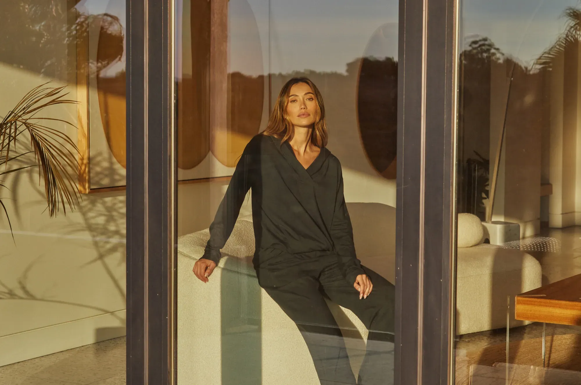A model in charcoal loungewear seen through glass at golden hour, Los Angeles
